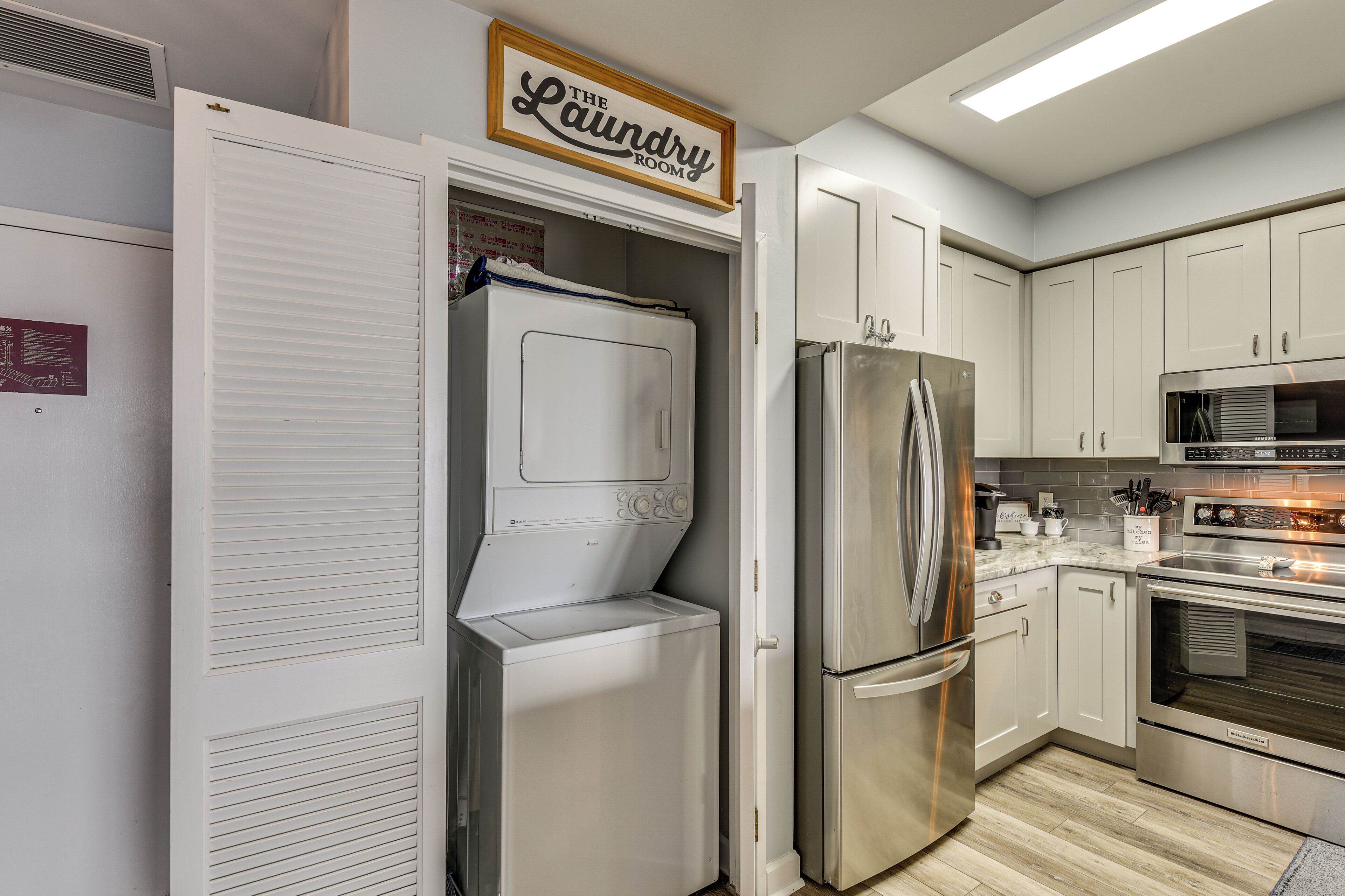 A compact kitchen with a built-in washer and dryer, stainless steel appliances, and a sign indicating the laundry room.