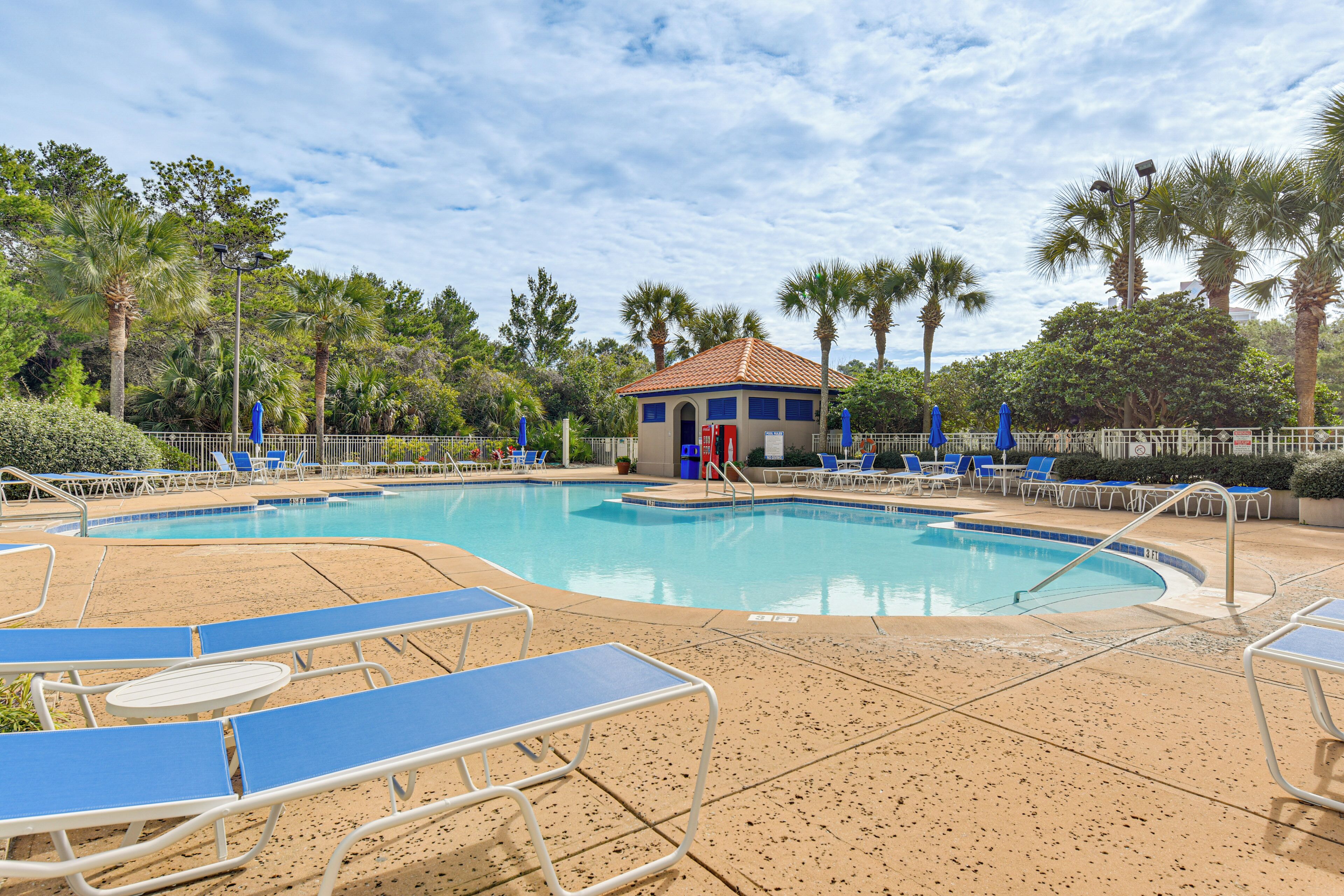 A swimming pool with blue lounge chairs and a small building with a red roof.