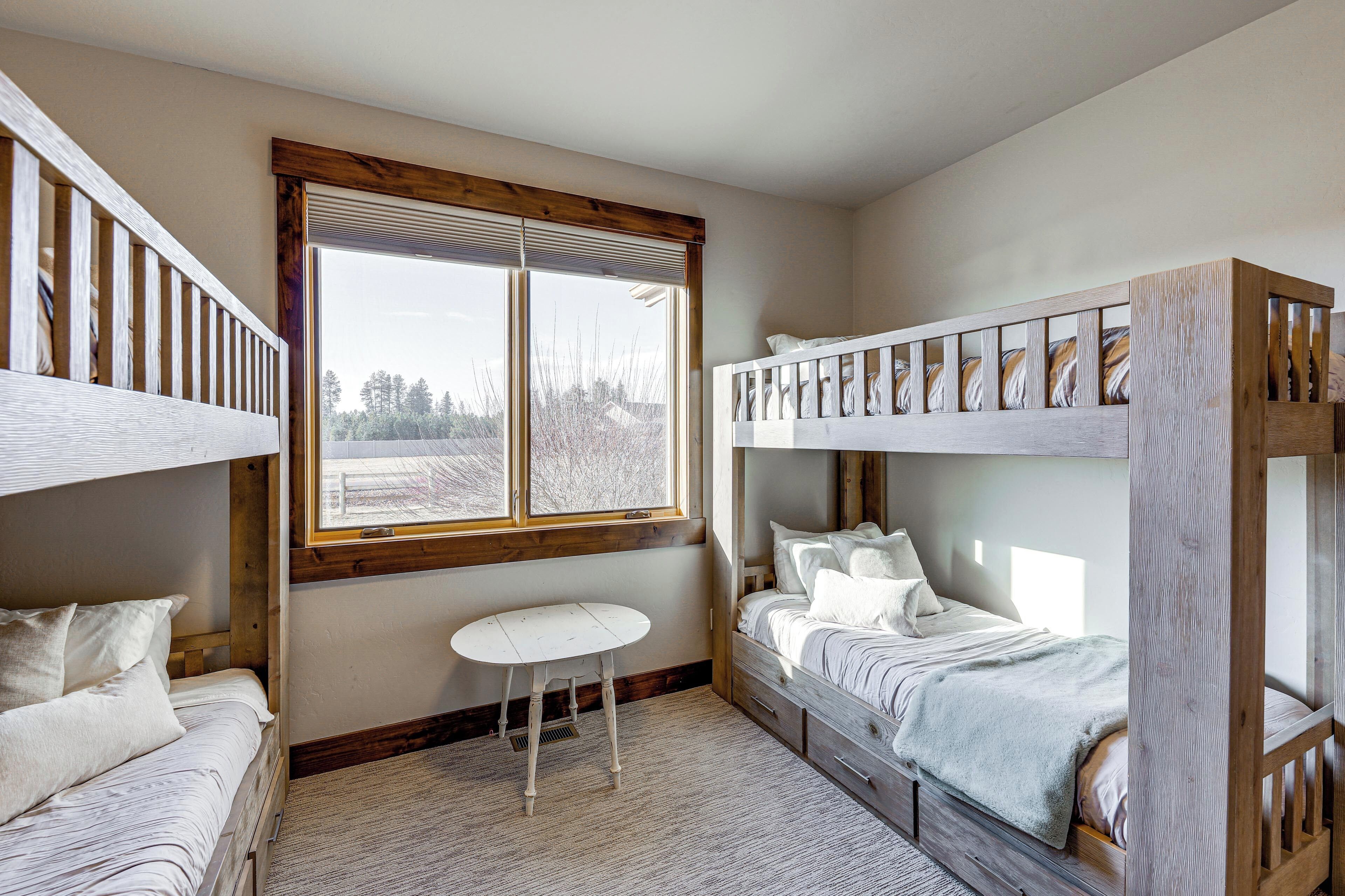 A bunk bed room with a window, a small table, and a bed with a white bedspread.