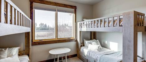A bunk bed room with a window, a small table, and a bed with a white bedspread.