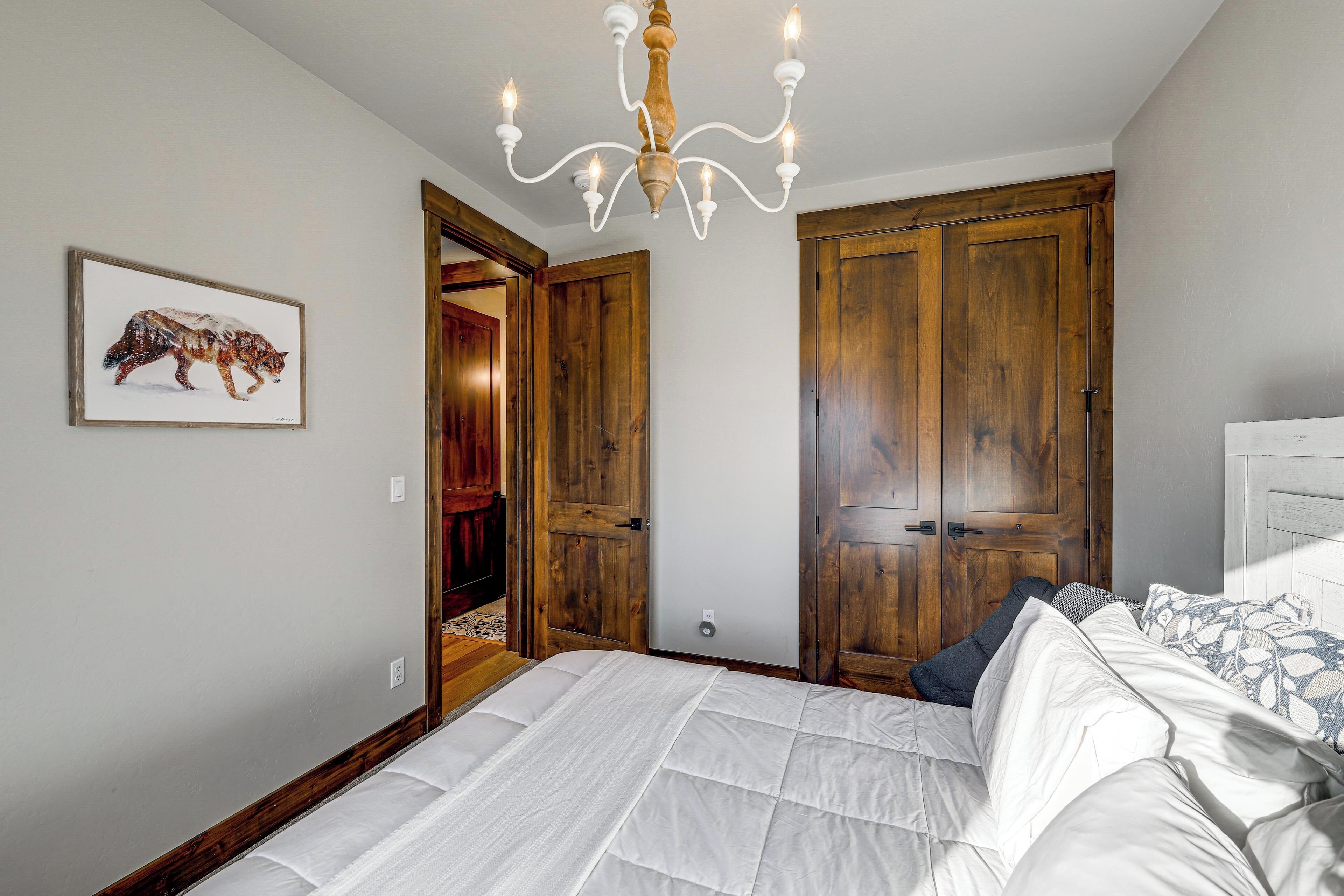 A bedroom with a large bed, wooden wardrobe, and a chandelier.