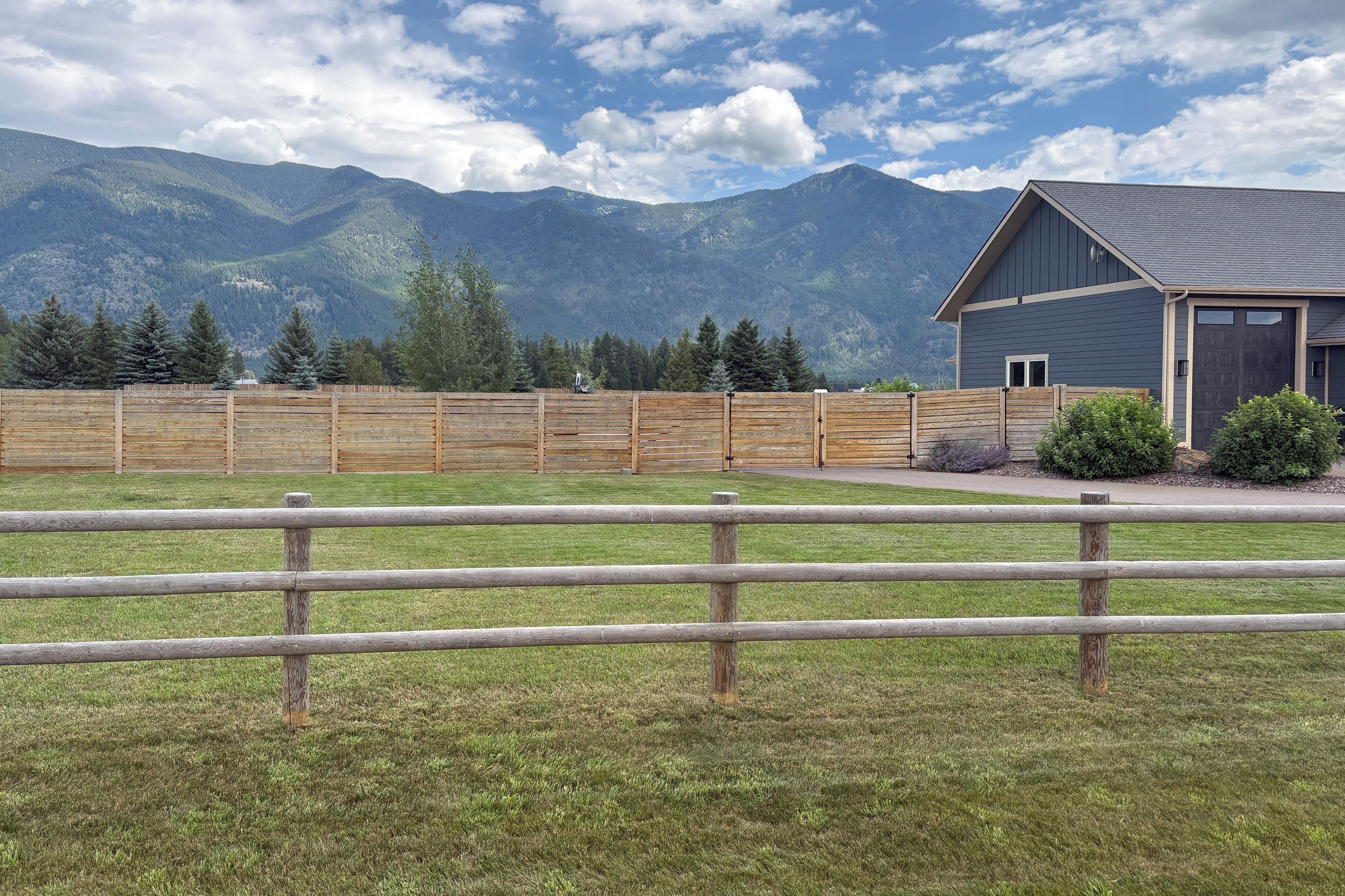 A fenced yard with a building, mountains in the background, and a clear sky.