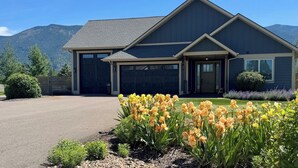 Une maison moderne à deux étages avec un garage, entourée d’une pelouse bien entretenue et de plantes en fleurs.