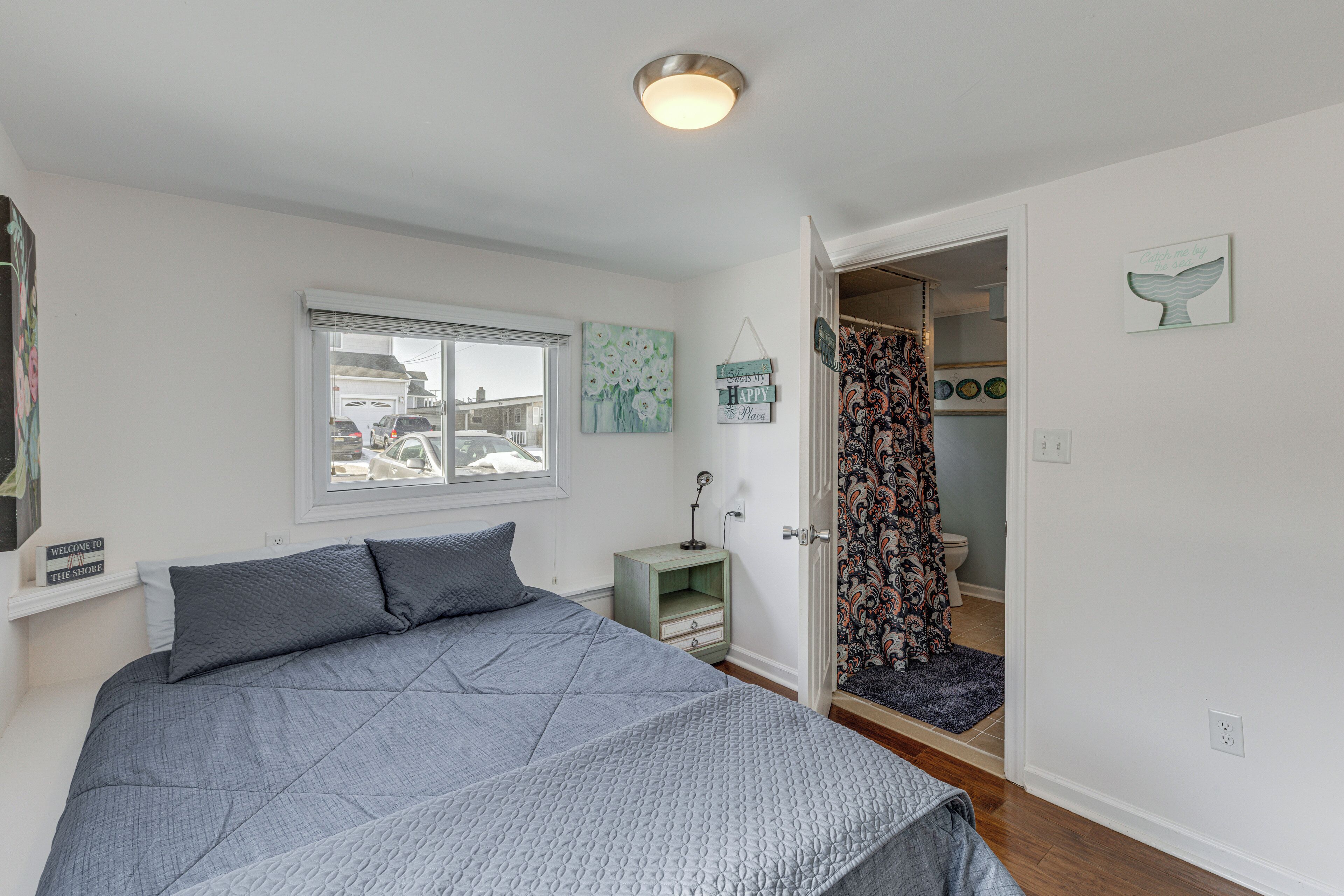 A bedroom with a bed, a nightstand, a window, and a door leading to a bathroom.