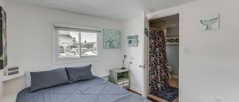 A bedroom with a bed, a nightstand, a window, and a door leading to a bathroom.
