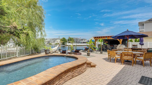 A swimming pool with a brick edge, outdoor furniture, and a barbecue area. - Canal-front Backyard Oasis! Jersey Shore Retreat (Brick)
