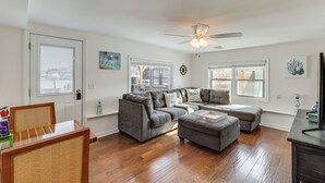 A spacious living room with hardwood flooring, a sectional sofa, a coffee table, and a ceiling fan. - Canal-front Backyard Oasis! Jersey Shore Retreat (Brick)