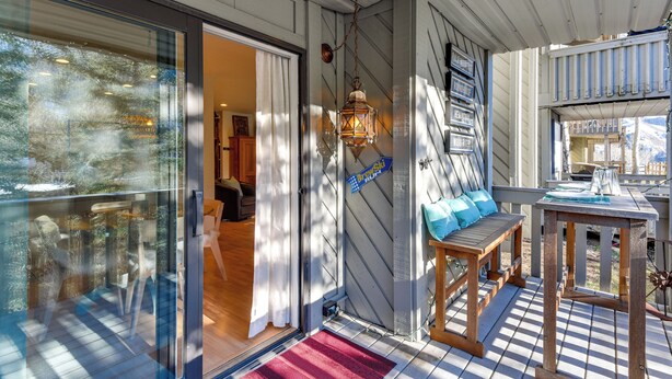 Un espace extérieur abrité, doté d’une table et d’un banc en bois, d’une lanterne suspendue et d’une porte en verre donnant sur l’intérieur.