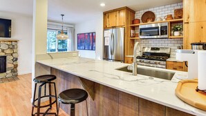 Une cuisine moderne dotée d’un grand îlot central, d’appareils électroménagers en acier inoxydable, d’armoires en bois et d’une cheminée en pierre.
