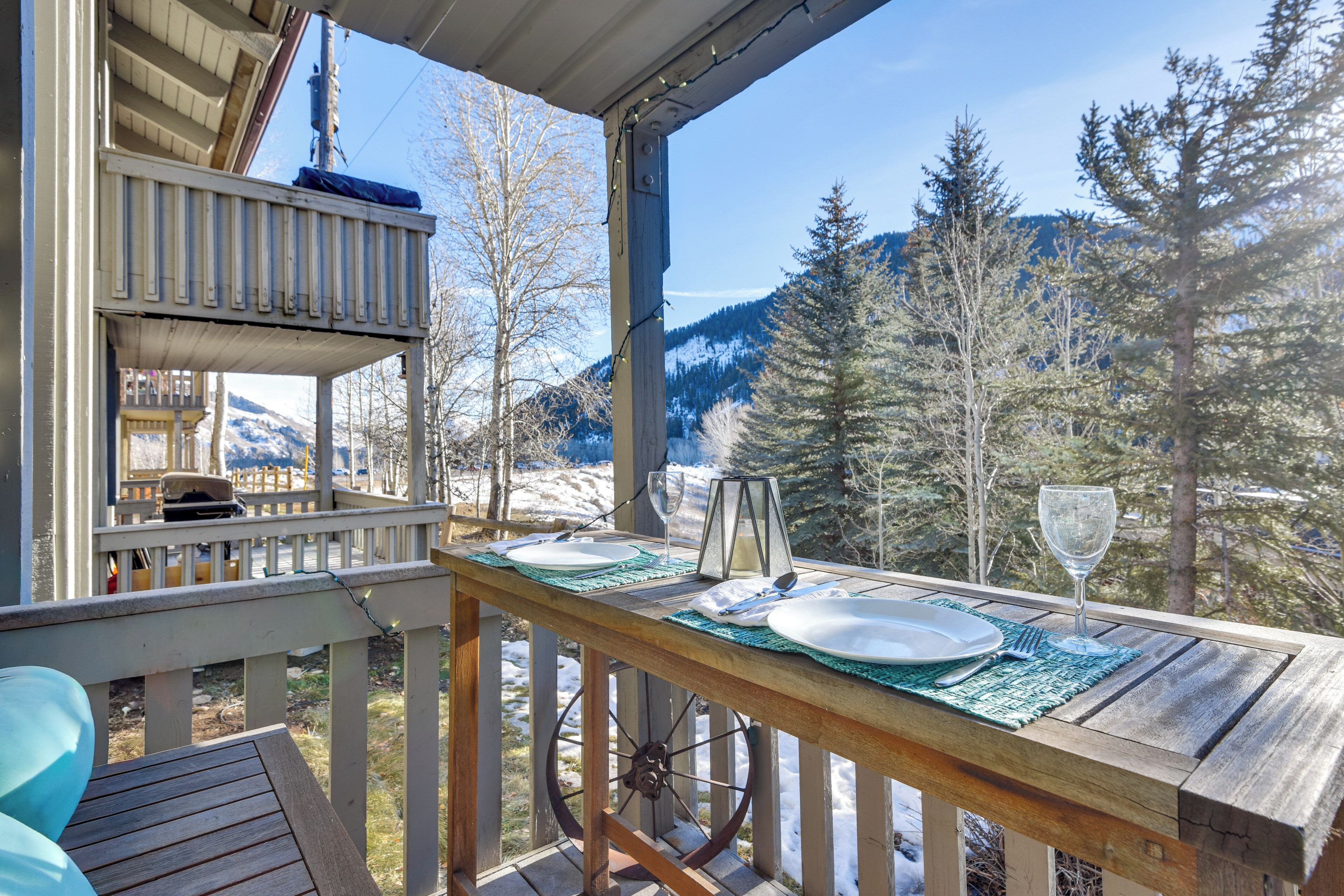 A wooden deck with a table set for two, overlooking a snowy mountain landscape.