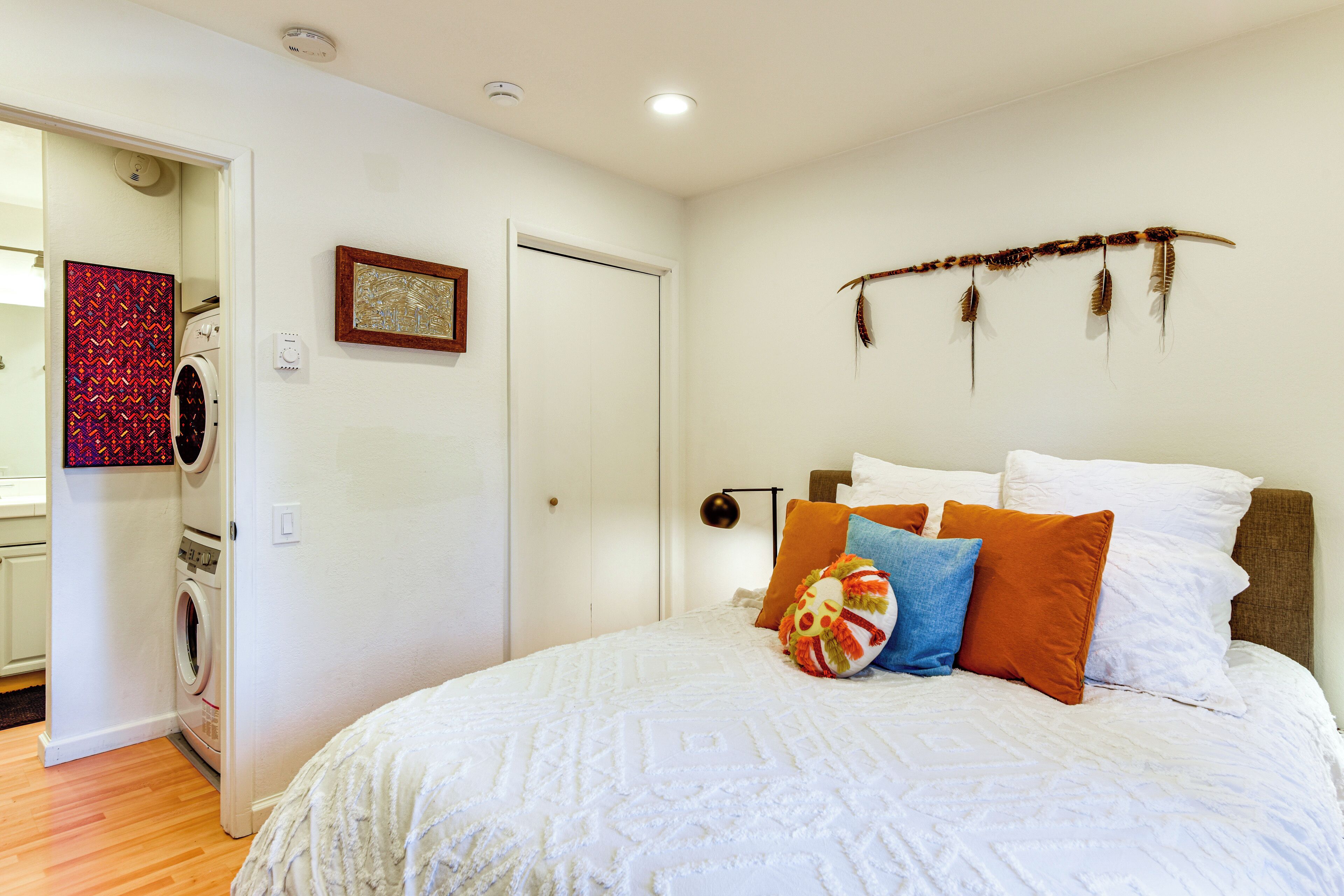 A bedroom with a bed, pillows, a wall-mounted artwork, and a door leading to a laundry area.