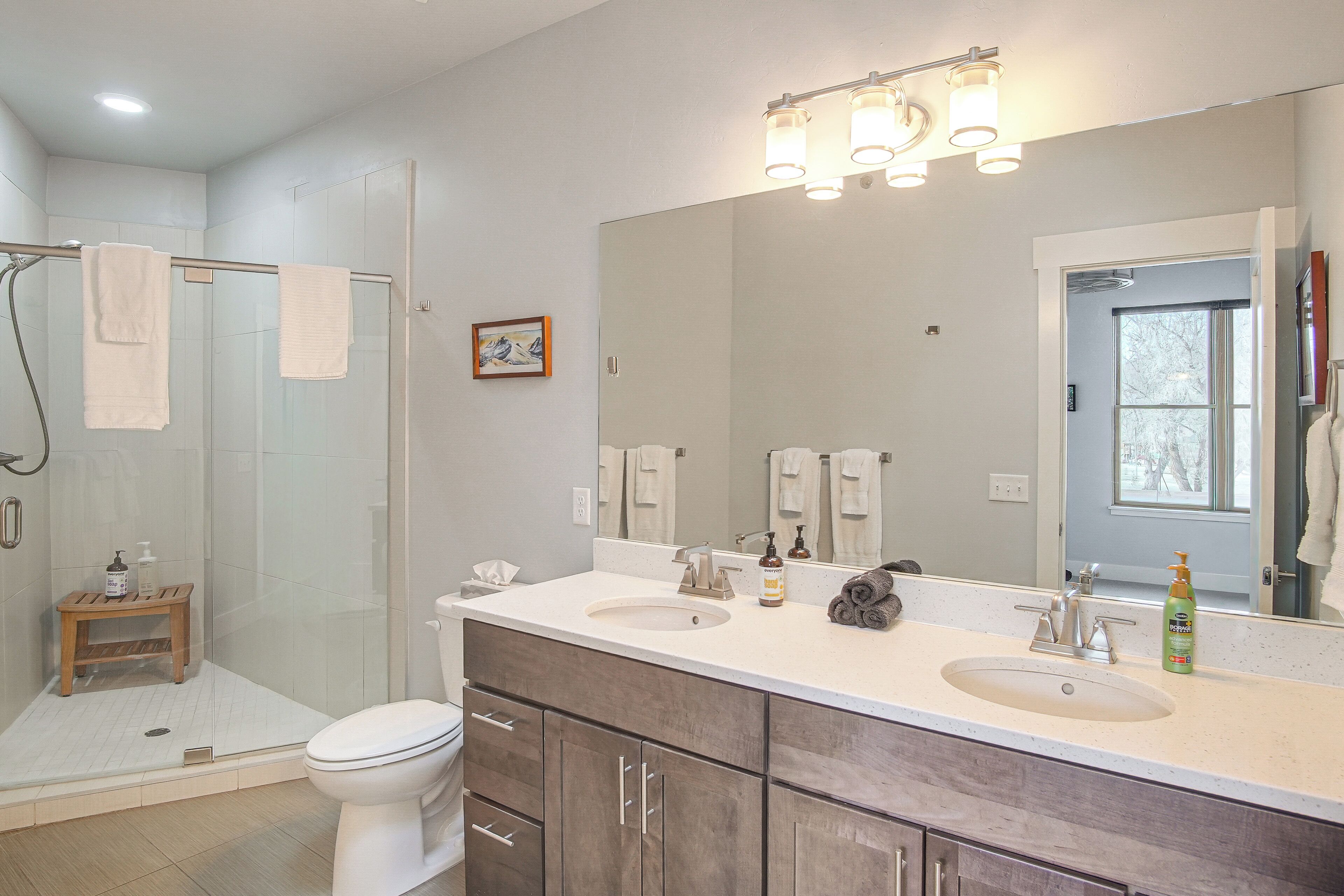 A modern bathroom with a glass shower enclosure, two sinks, a large mirror, and a toilet.