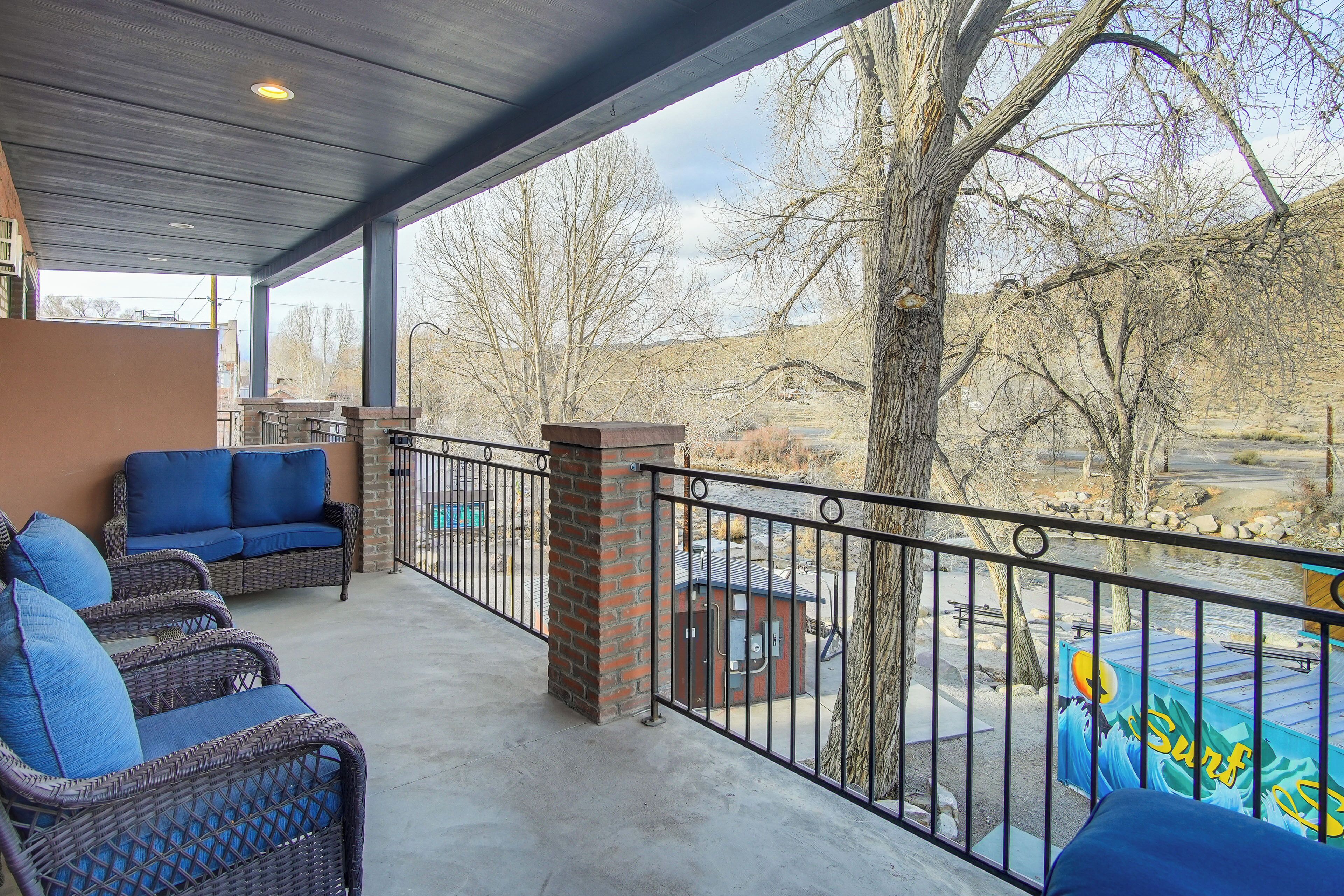 A covered outdoor seating area with wicker furniture and a view of a river and mountains.