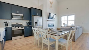 A modern kitchen with dark cabinets, a microwave, stove, and refrigerator. There is a dining table with chairs and a gray sofa in the background. - Great for Boating & Fishing! Lake Greenwood Escape (Greenwood)