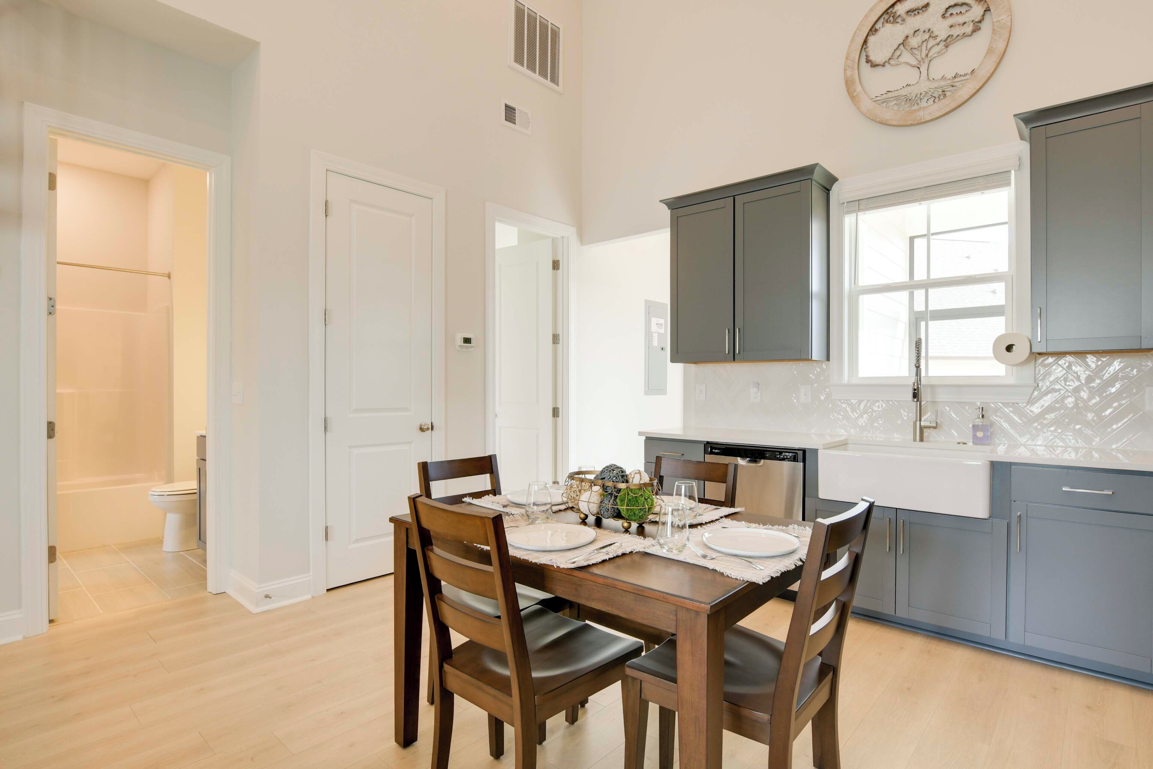 A modern kitchen with grey cabinets, a white countertop, and a dining area with a wooden table and chairs.