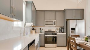 A modern kitchen with grey cabinets, a white countertop, stainless steel appliances, and a dining area with wooden chairs. - Steps to Marina! Lake Greenwood Home w/ Patios (Greenwood)