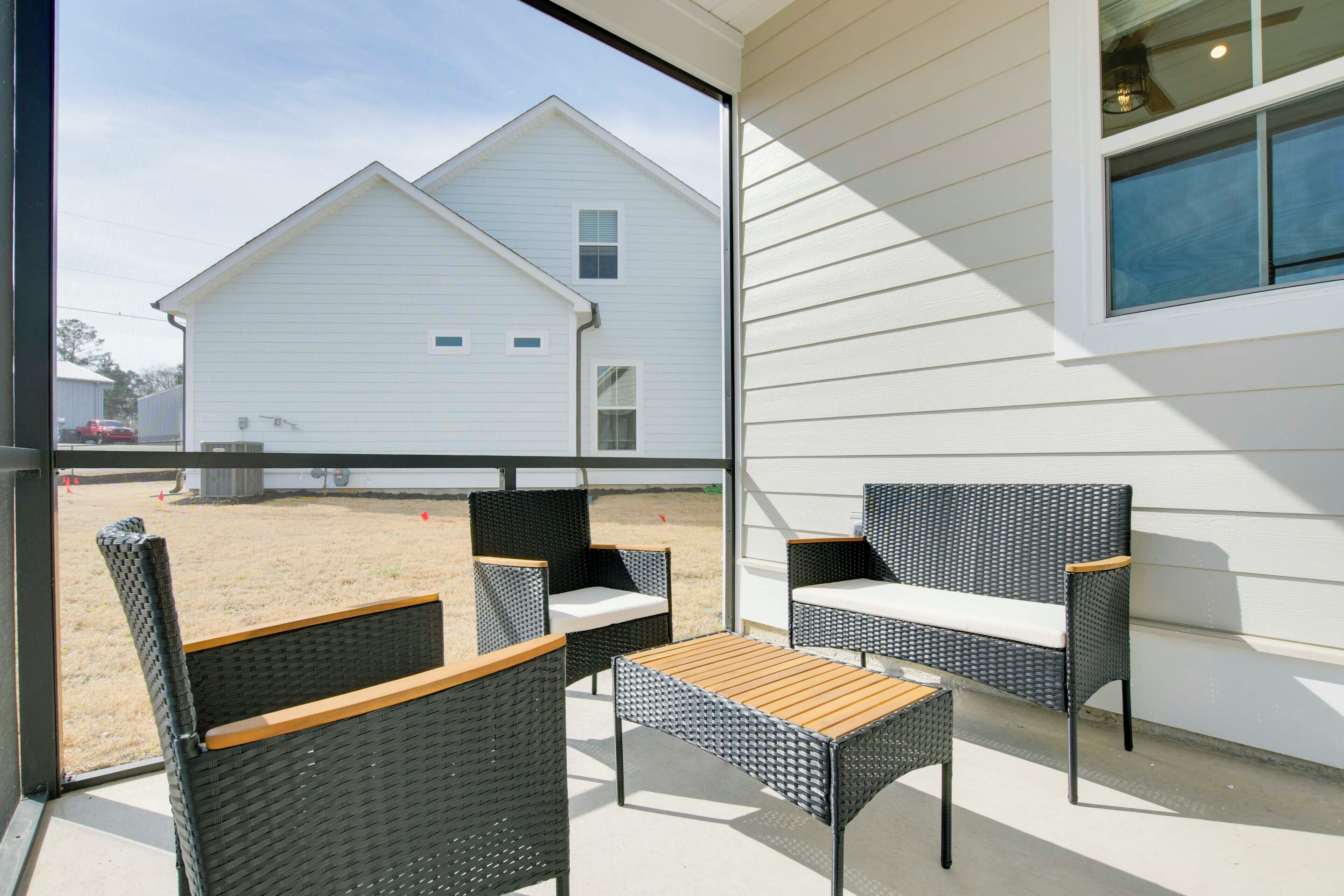 An outdoor seating area with wicker furniture and a wooden table, overlooking a white building and a grassy yard.