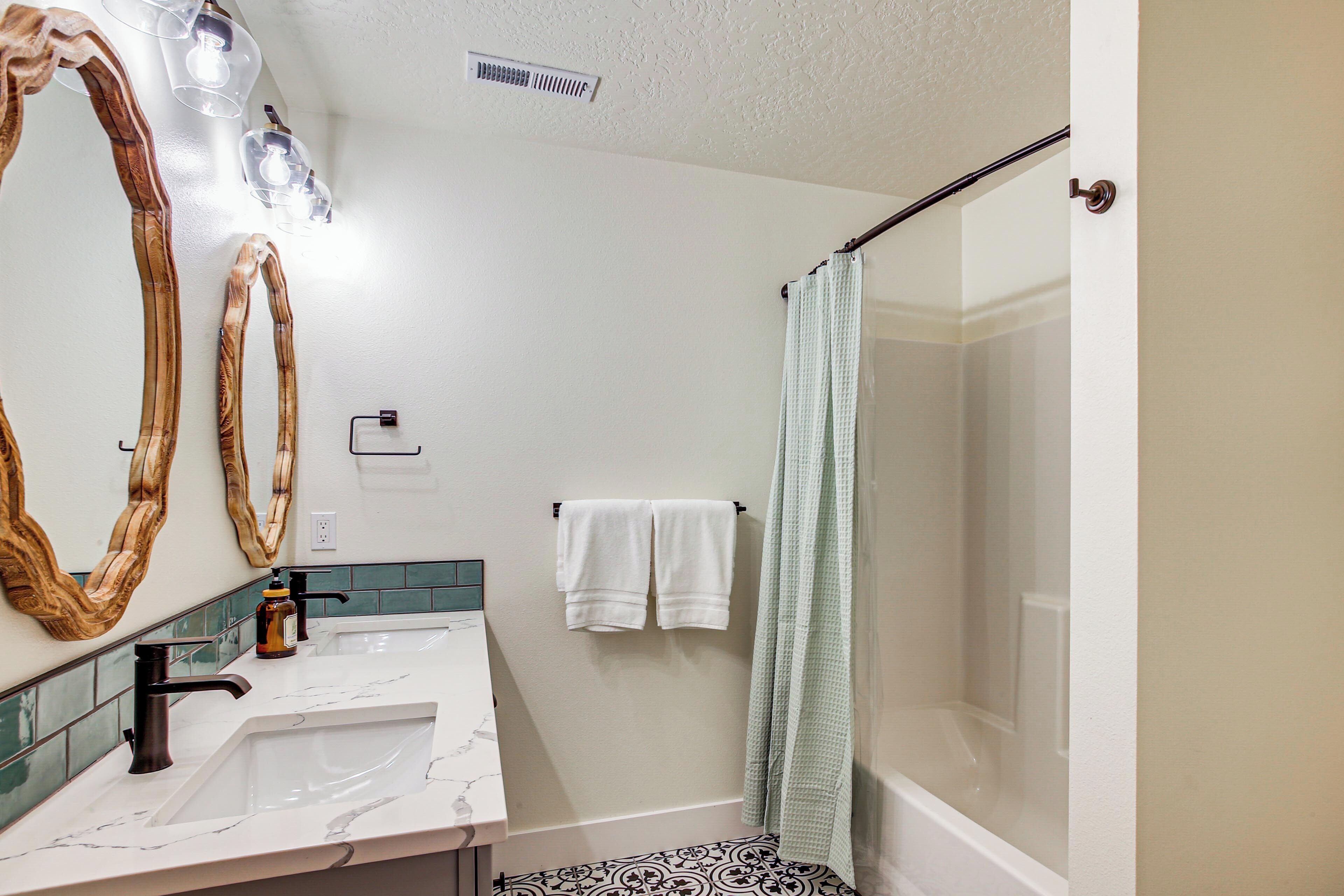 Une salle de bain avec un lavabo blanc, deux miroirs, un rideau de douche et un porte-serviettes.