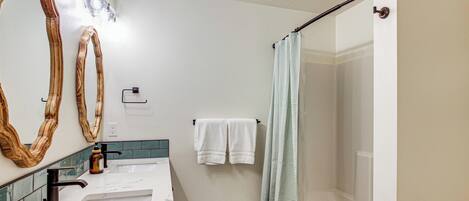 Une salle de bain avec un lavabo blanc, deux miroirs, un rideau de douche et un porte-serviettes.