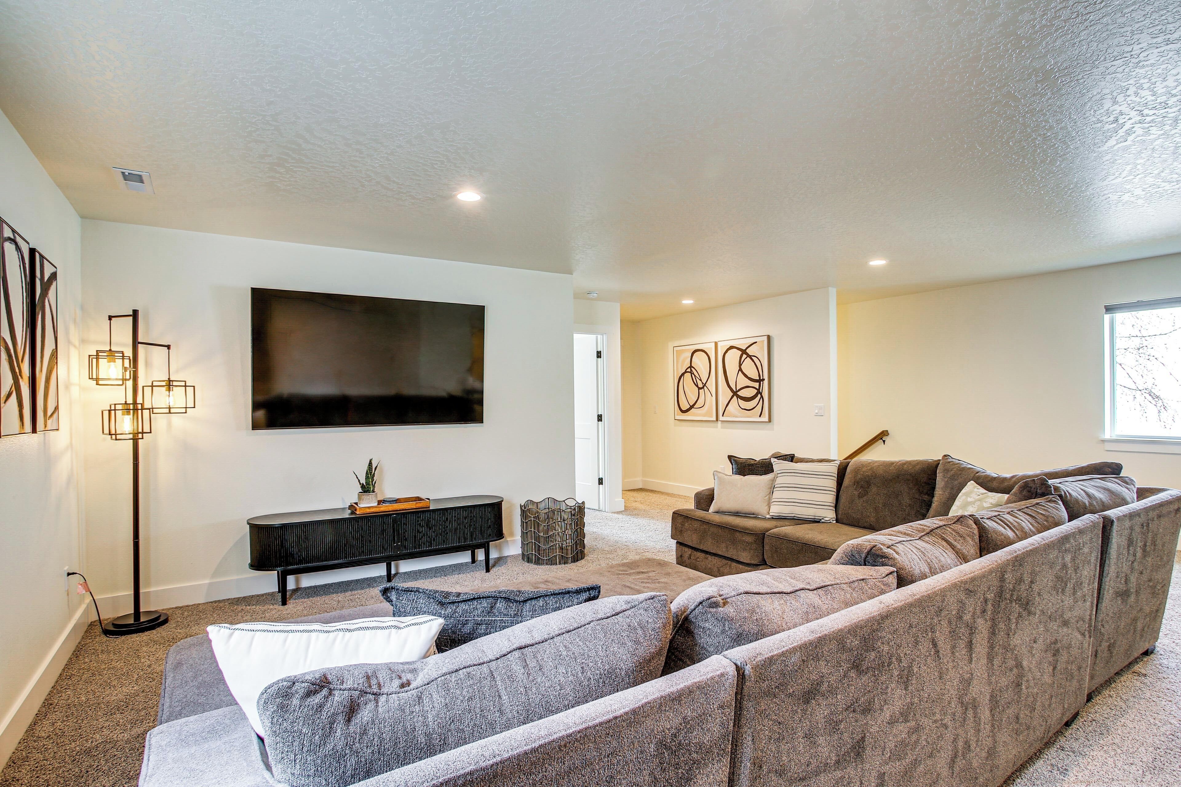 A modern living room with a large sectional sofa, a flat-screen TV mounted on the wall, a console table, and abstract wall art.