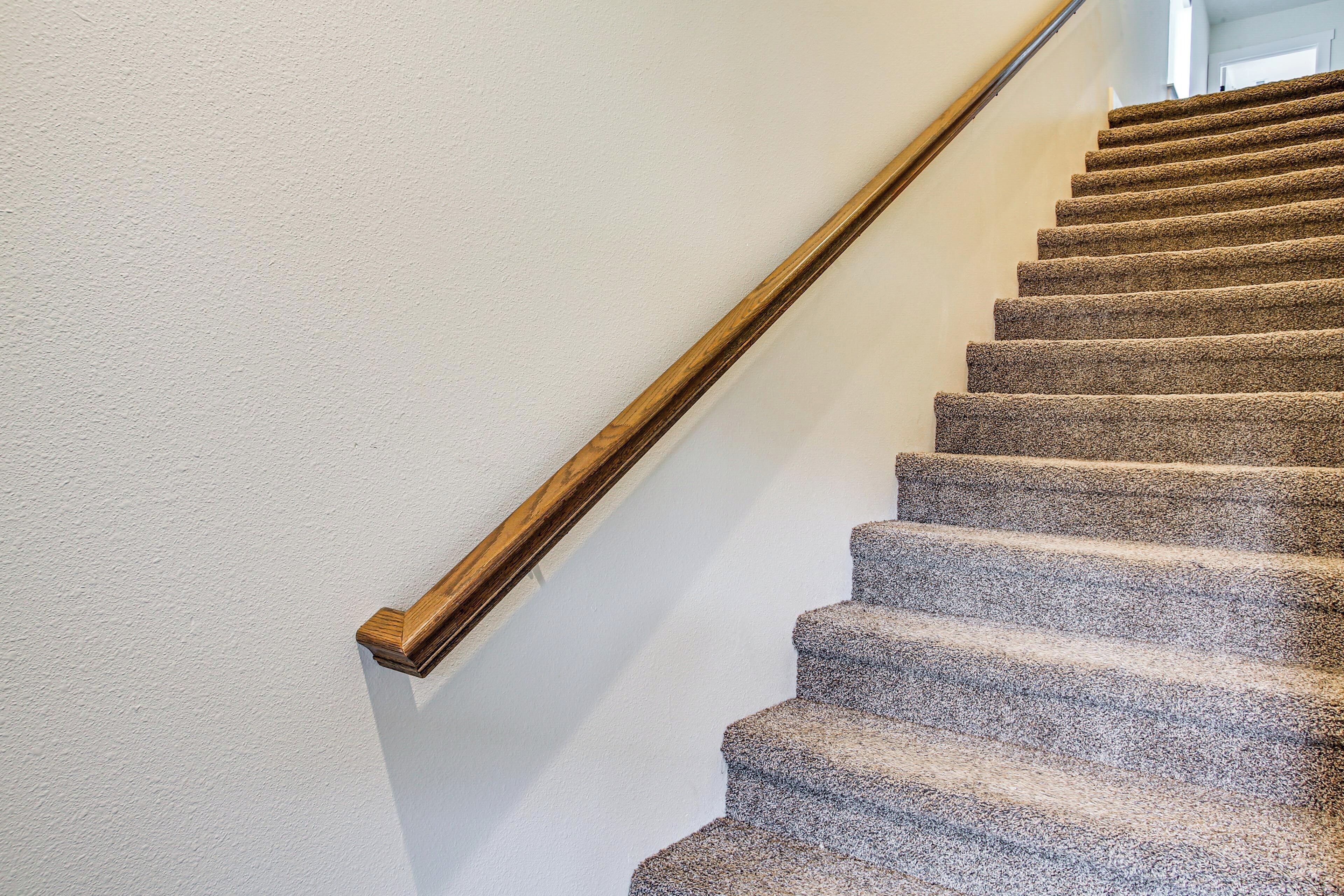 A carpeted staircase with wooden handrails against a plain wall.
