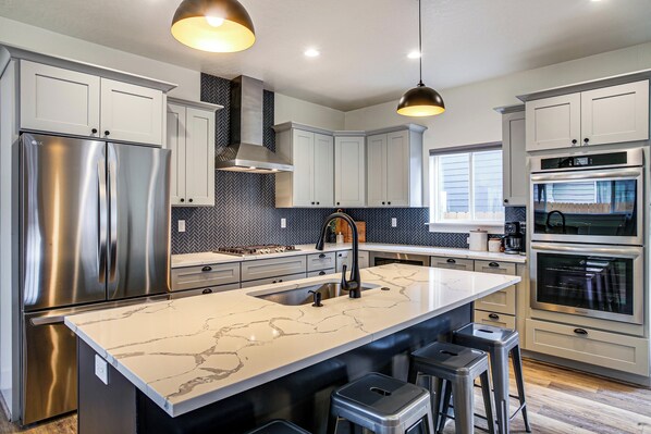 A modern kitchen with stainless steel appliances, a marble island, and pendant lighting.