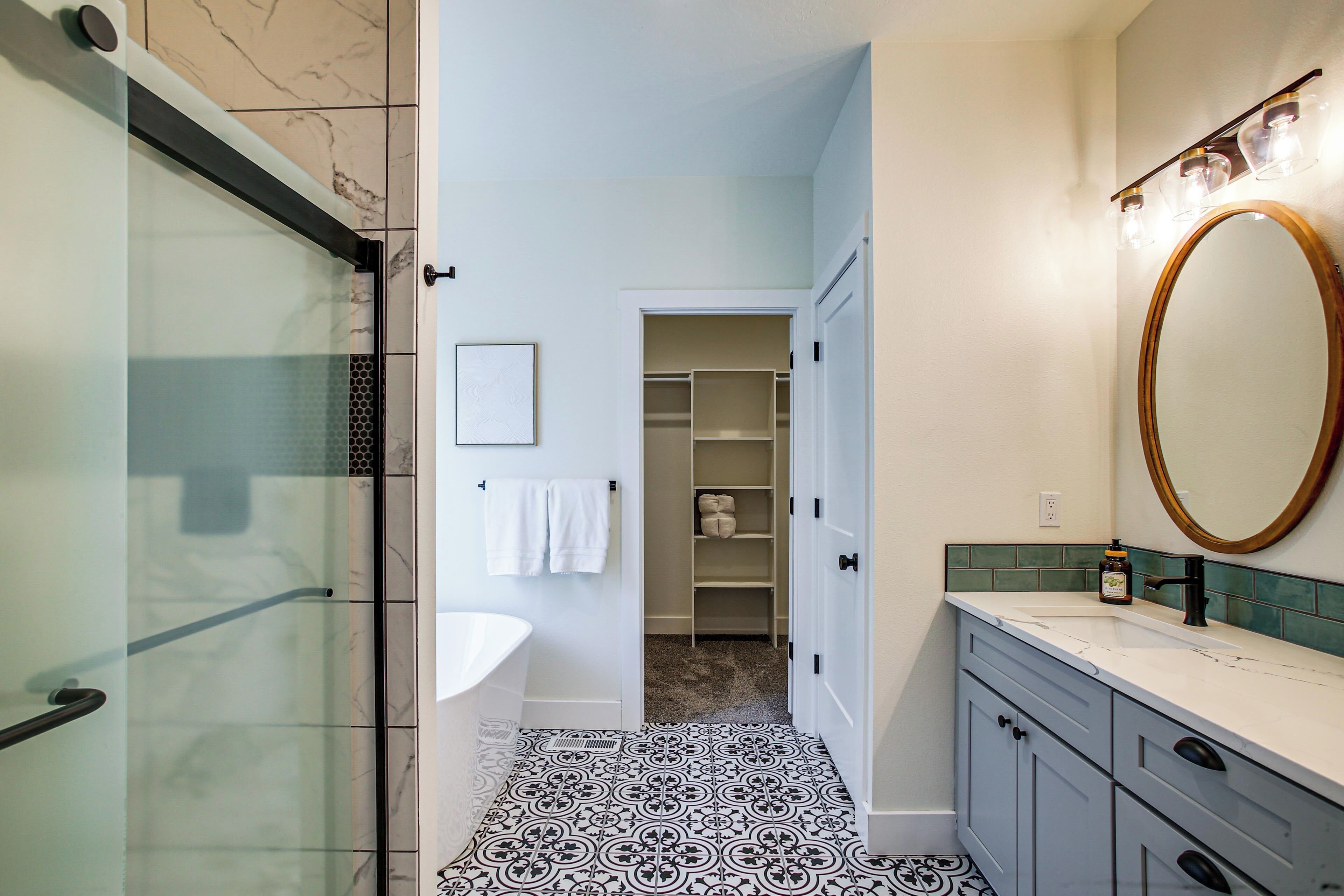 Un baño con cabina de ducha de vidrio, un lavabo blanco, un espejo con marco de madera y suelo de baldosas.