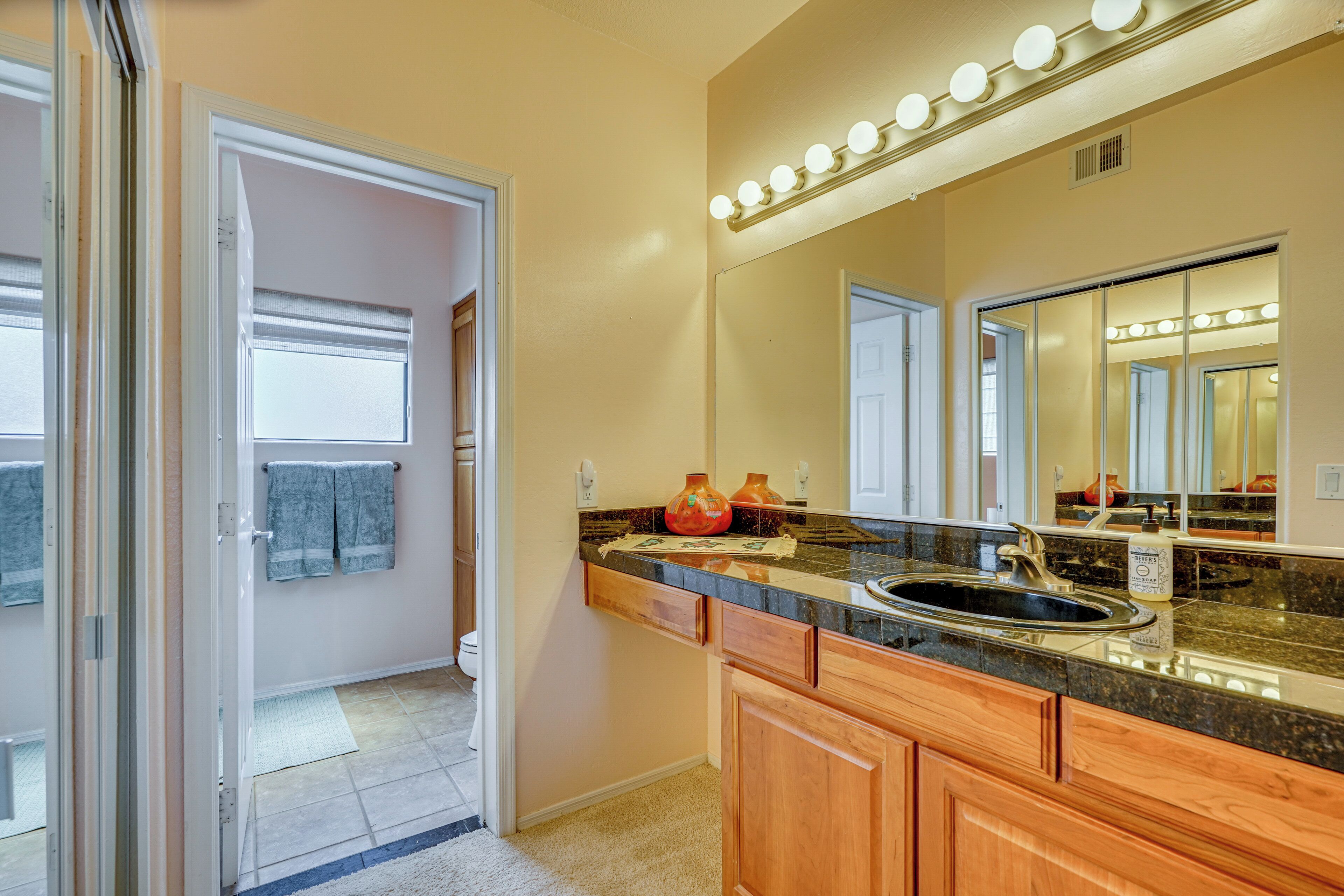 A bathroom with a vanity, sink, and mirror. There are lights above the mirror and a towel rack with towels.