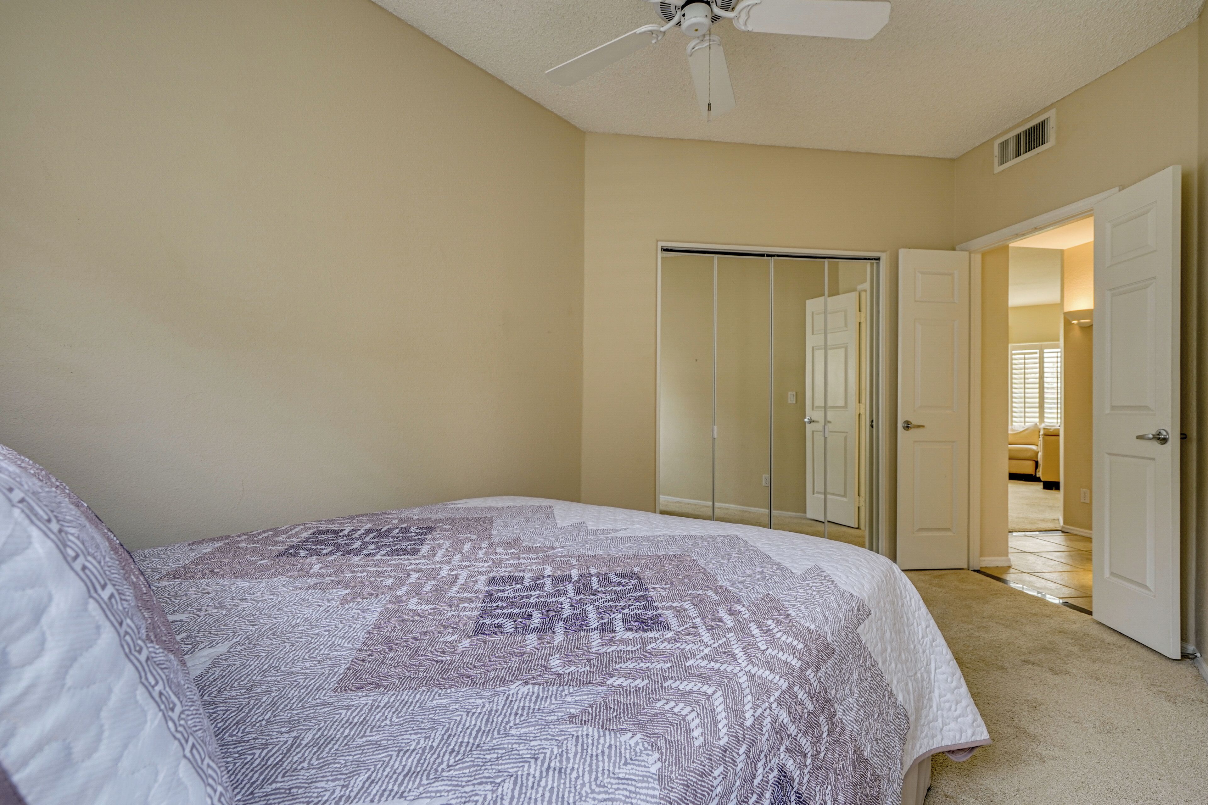 A bedroom with a bed, a ceiling fan, a walk-in closet, and a door leading to another room.