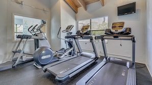 Un gimnasio con cintas de correr, elípticas y un televisor montado en la pared.