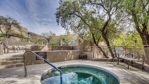Un jacuzzi con escalera de metal, rodeado por una terraza de concreto y una valla de metal.