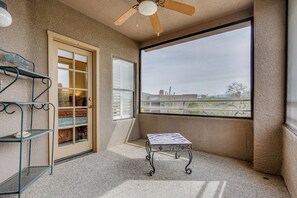 Quarto com uma grande janela, ventilador no teto, porta com painéis de vidro e mesa de metal.