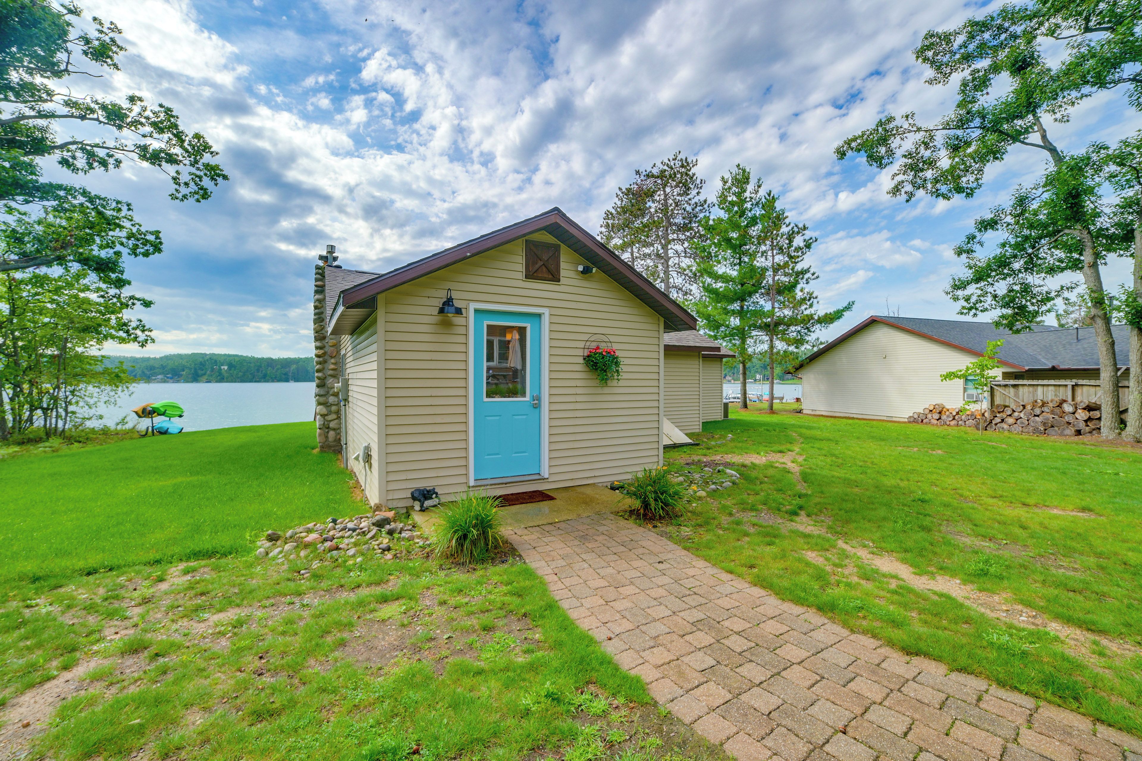 A small cabin with a blue door, a stone chimney, and a view of a lake.