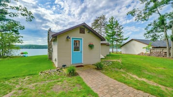 A small cabin with a blue door, a stone chimney, and a view of a lake.
