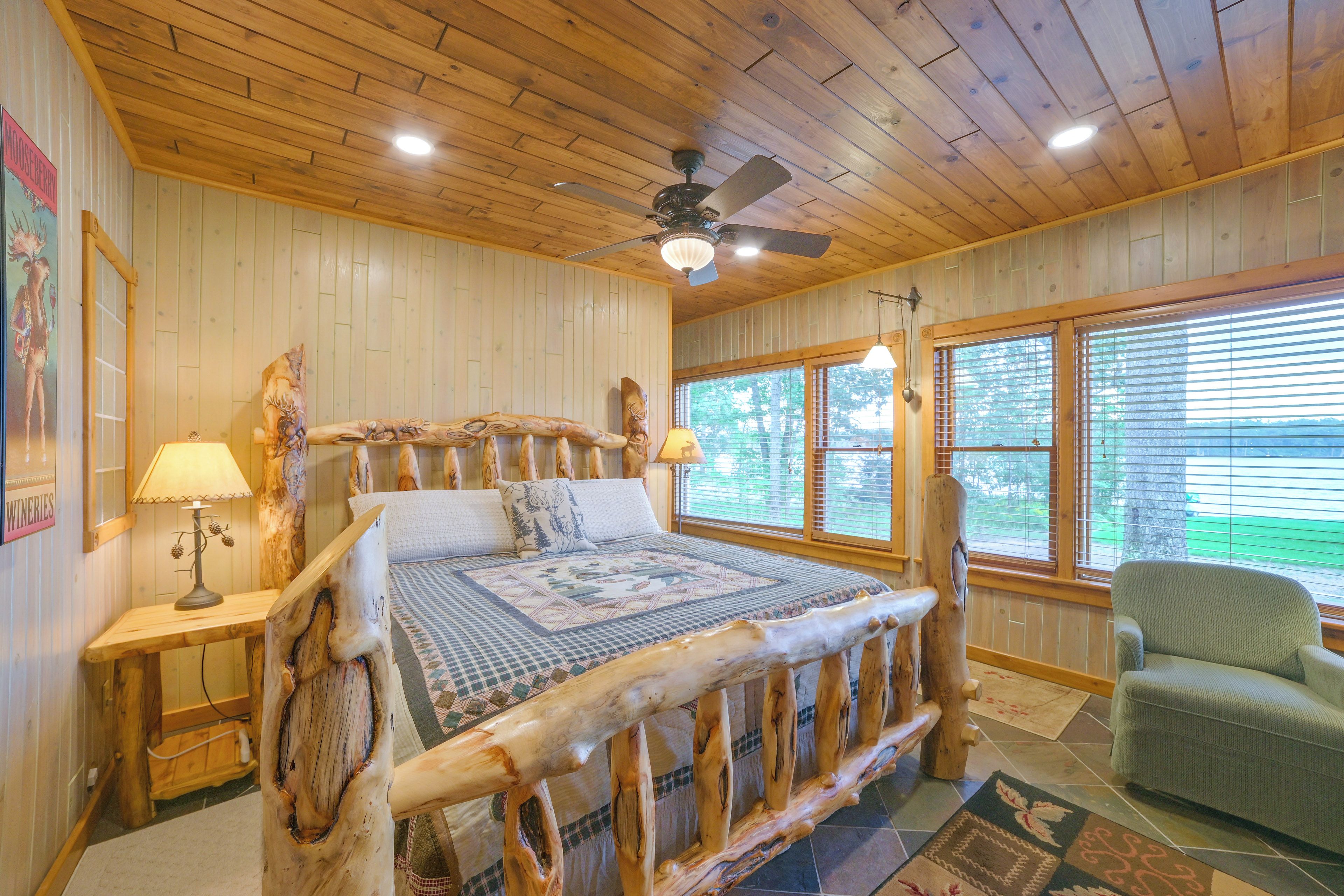 A wooden cabin bedroom with a large bed, a ceiling fan, and a window with blinds.