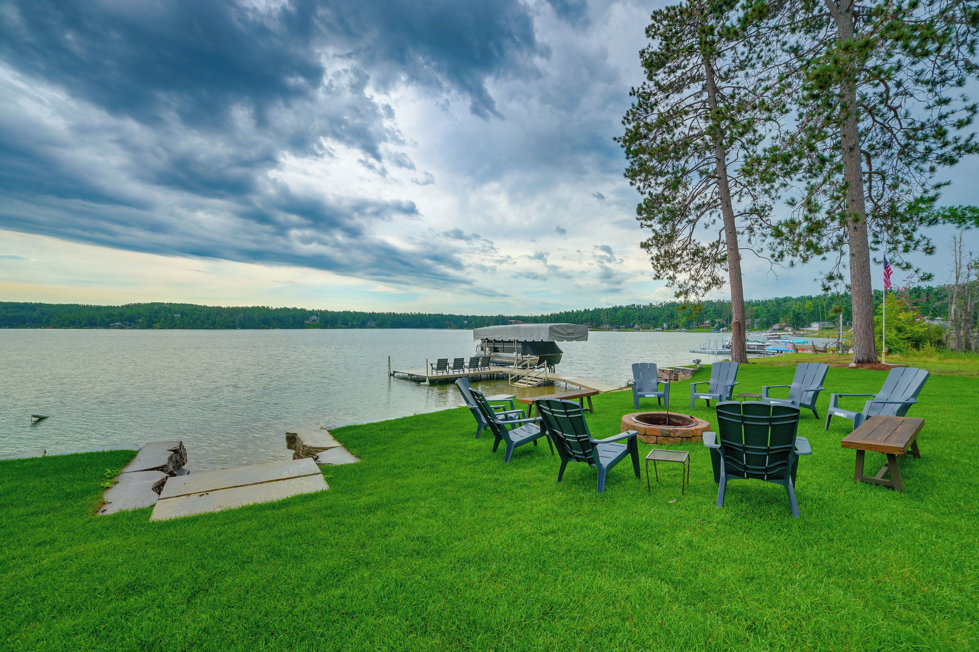 A lakeside patio with outdoor seating, a dock, and a view of the lake and distant trees.