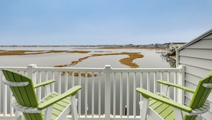 Un balcon avec deux chaises vertes et une vue sur une étendue d’eau bordée de zones marécageuses.