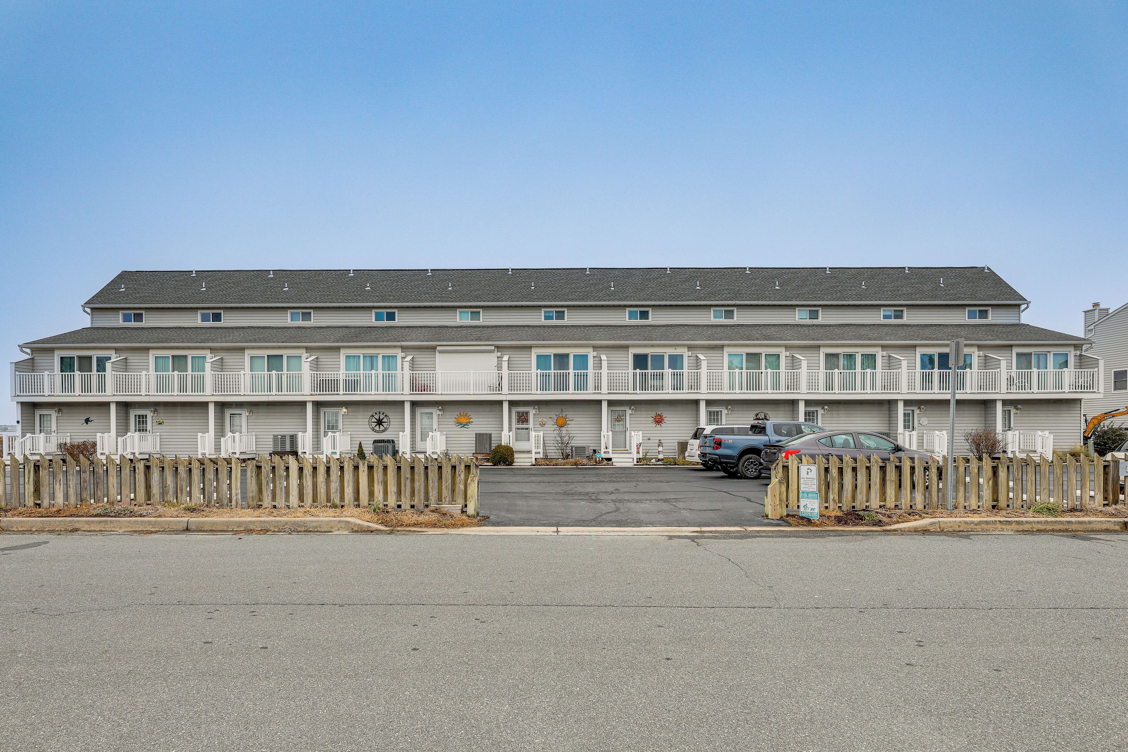 Een motel met meerdere verdiepingen, een centrale ingang, een parkeerplaats en een houten omheining.