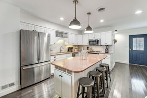 A modern kitchen with stainless steel appliances, a central island with stools, and a blue door. - 1 Mi to Fenwick Island SP: Condo w/ Boat Dock! (Selbyville)