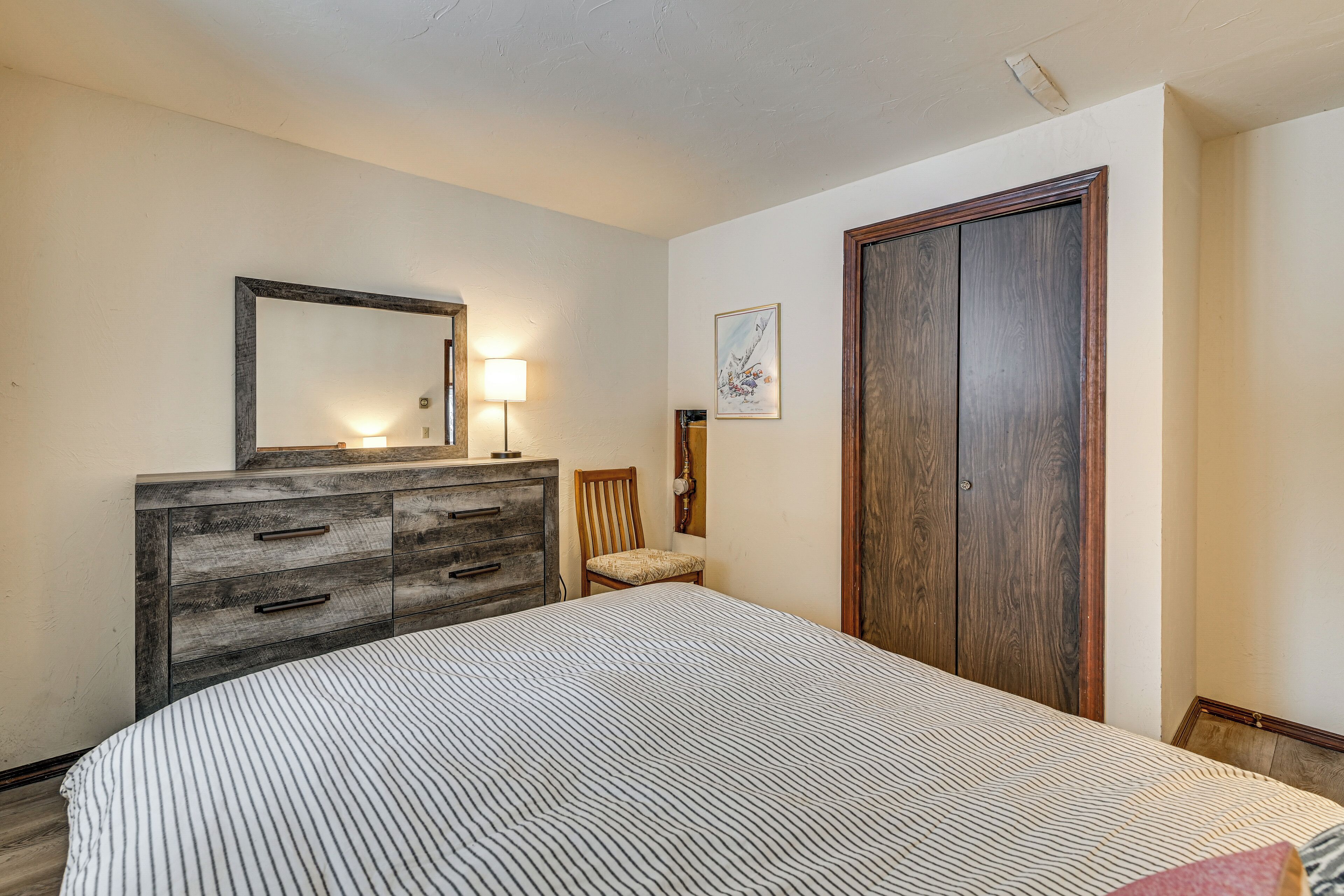 A bedroom with a bed, a wooden dresser, a chair, a large mirror, and a door.