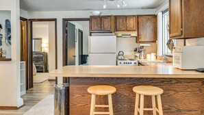 A kitchen with wooden cabinets, a large island with stools, a refrigerator, a stove, and a trash can. - 3 Mi to Windham Mountain: Pet-friendly Apt w/ Yard (Hensonville)