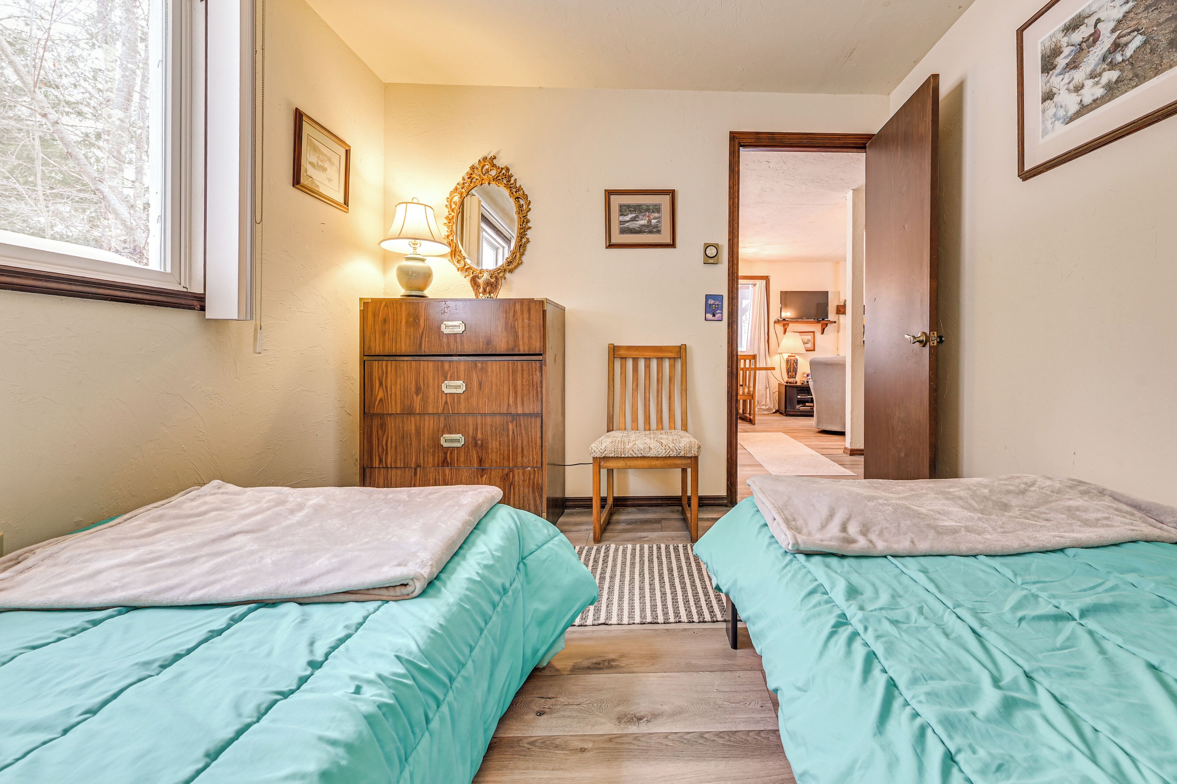 A bedroom with two beds, a wooden dresser, a chair, and a door leading to a bathroom.