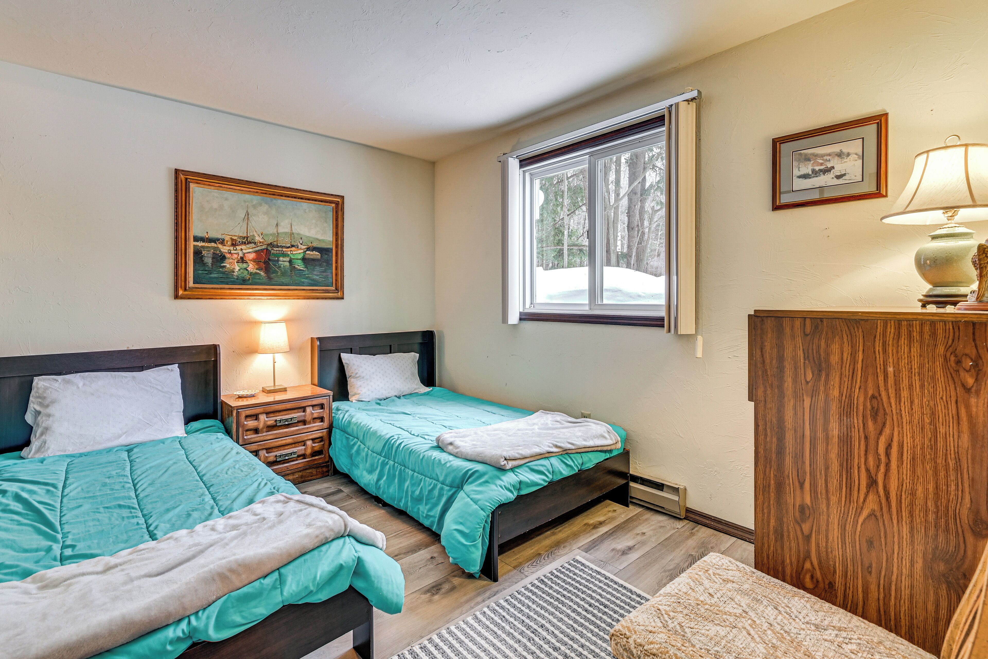 A bedroom with two beds, a nightstand, a lamp, a painting, and a window.