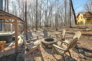 Une terrasse en bois avec des fauteuils Adirondack et un foyer en pierre, le tout entouré d’une forêt.