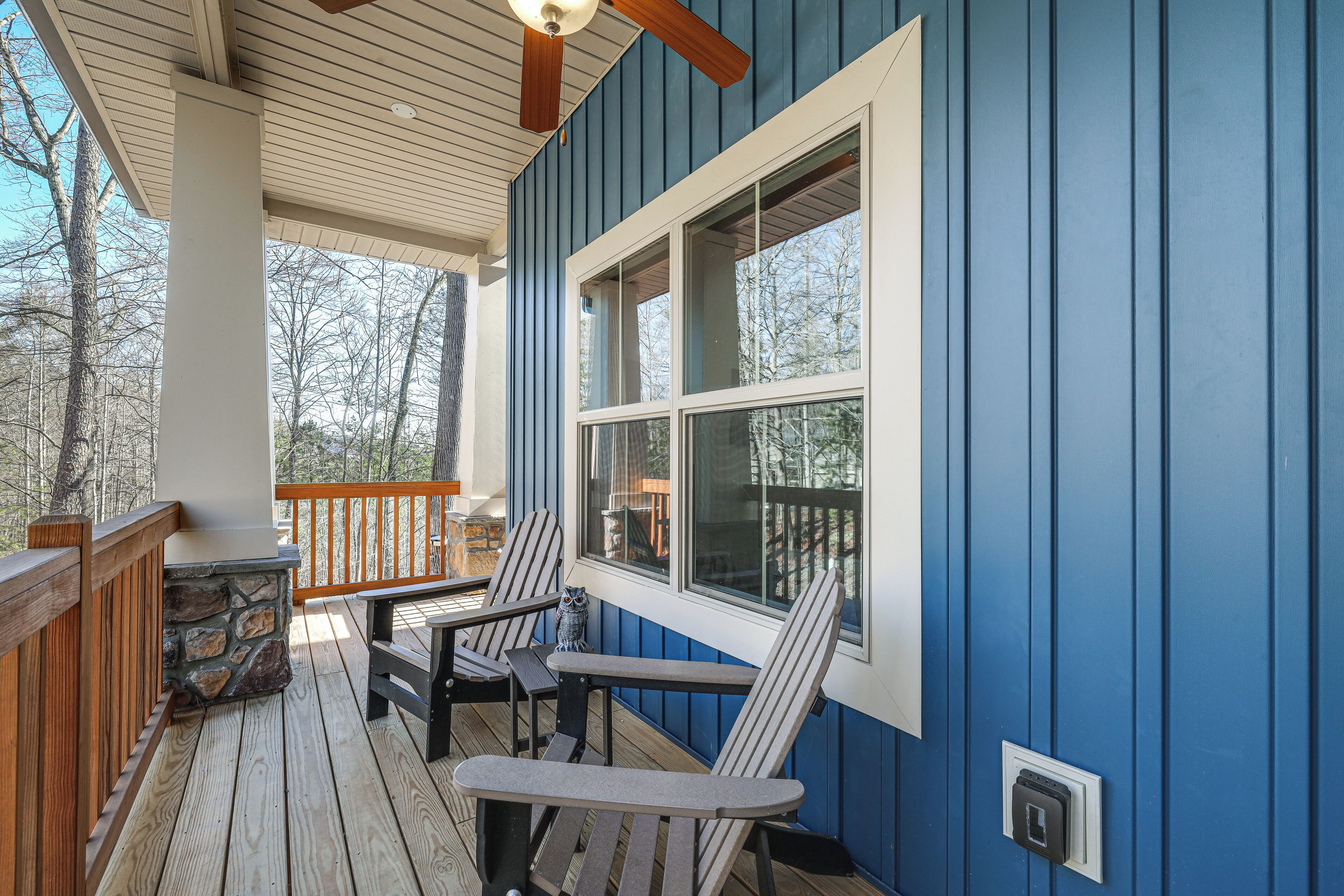 A covered porch with Adirondack chairs, a stone fireplace, and a view of trees.