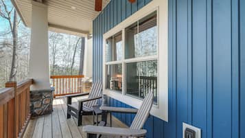 A covered porch with Adirondack chairs, a stone fireplace, and a view of trees.