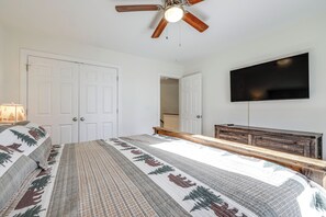 Une chambre à coucher comprenant un lit, un ventilateur de plafond, un téléviseur fixé au mur et une commode.