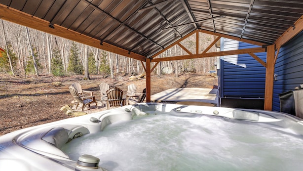 A hot tub under a metal roof with wooden chairs and a view of trees. - Lake Lure Getaway w/ Hot Tub & Fire Pit! (Lake Lure)