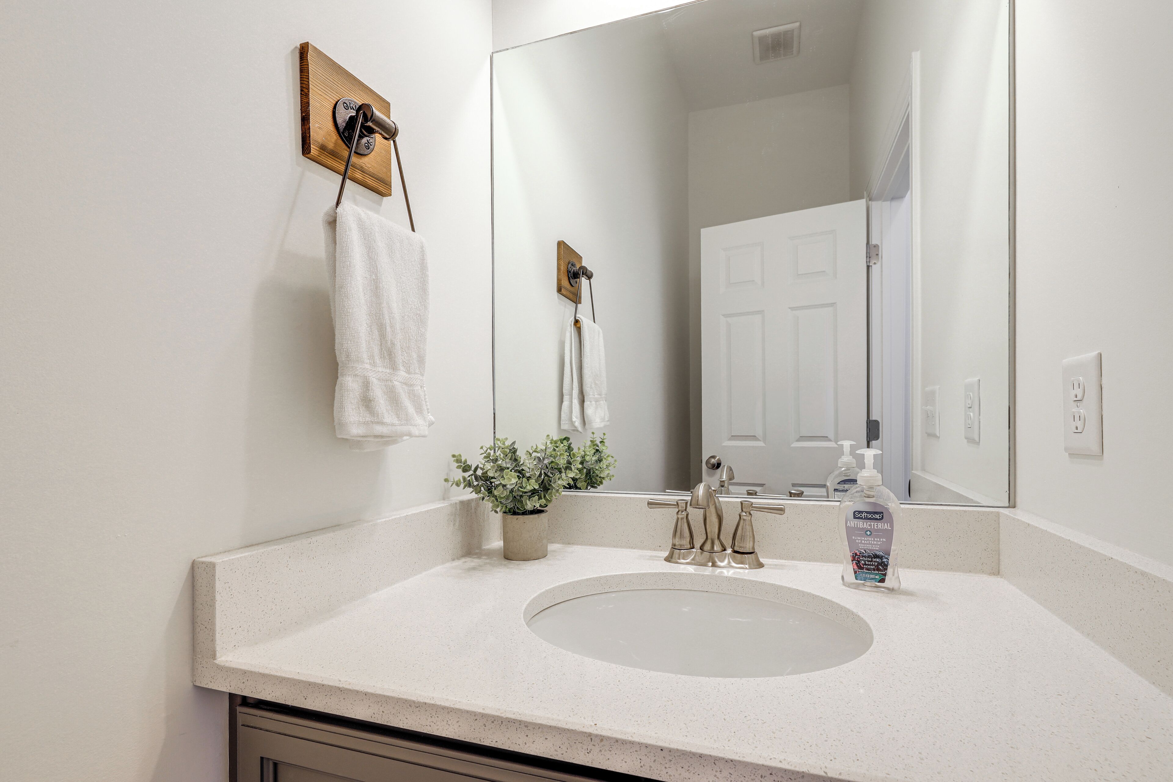 A bathroom with a white sink, a mirror, a towel rack, and a potted plant.