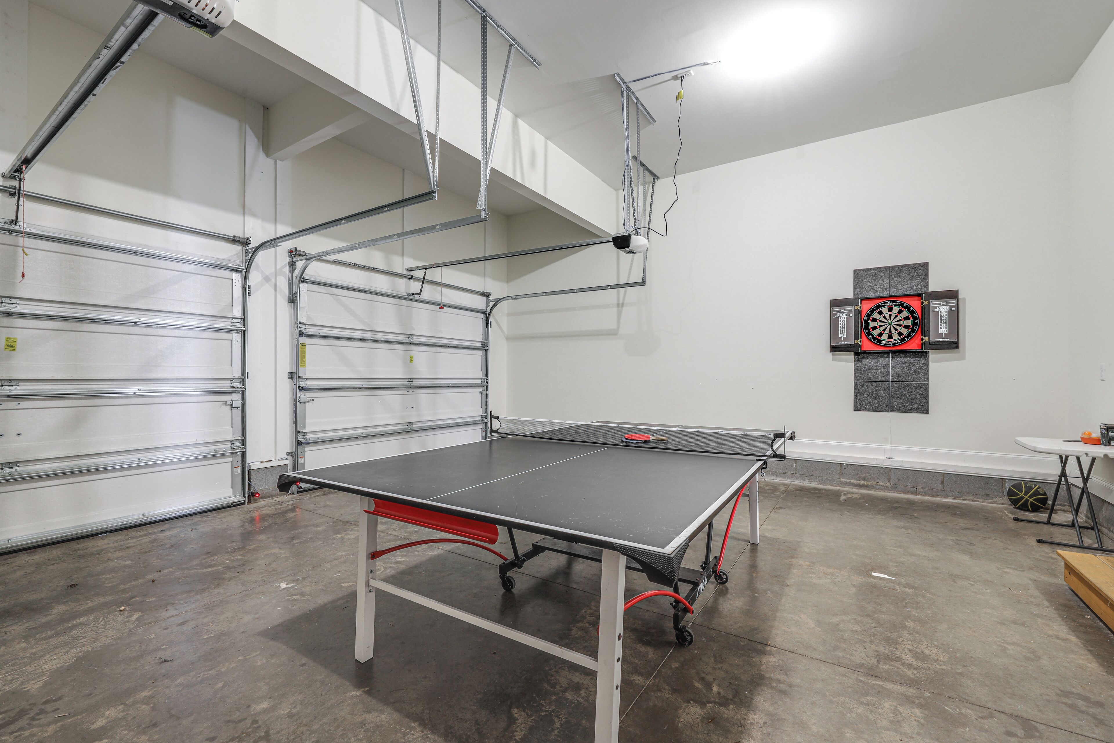 Una mesa de ping pong en un amplio espacio interior con estanterías metálicas y un dardo en la pared.
